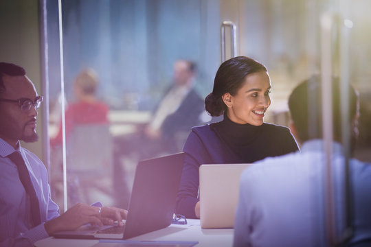 Smiling businesswoman at laptop listening in conference room meeting