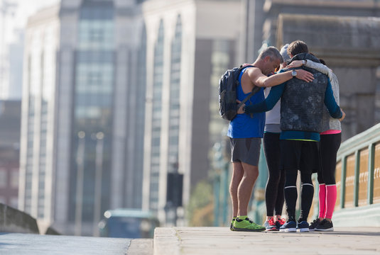 Runners connected in a huddle on sunny urban sidewalk
