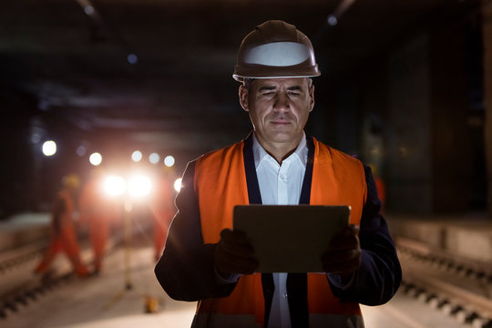 Serious male foreman using digital tablet at dark construction site