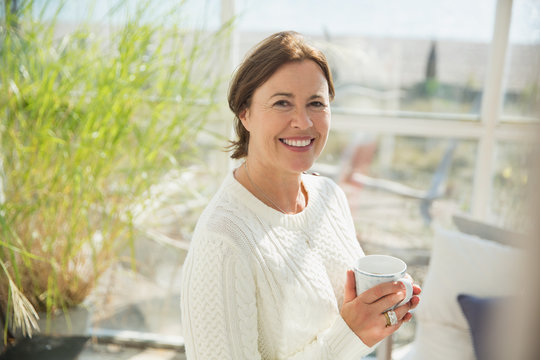 Portrait smiling mature woman drinking coffee in sunny sunroom