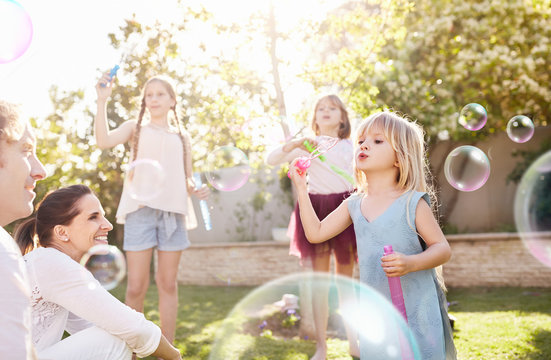 Parents watching daughters blowing bubbles in sunny back yard