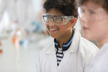 Smiling boy wearing goggles and lab coat in laboratory classroom