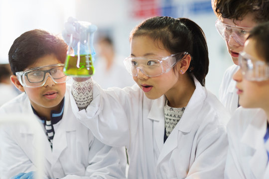 Curious students examining liquid in beaker, conducting scientific experiment in laboratory classroom