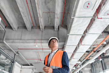 Foreman with clipboard looking up at construction site