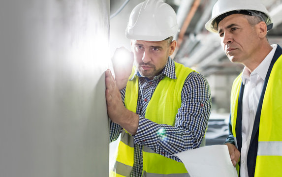 Male engineer flashlight examining underground wall at construction site