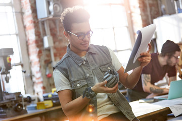 Young male designer examining prototype and notes in workshop