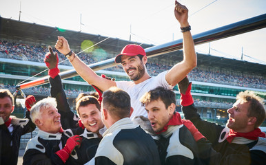 Formula one racing team carrying driver on shoulders, celebrating victory