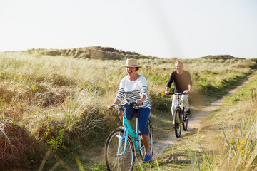 Mature couple riding bicycles on sunny beach grass path