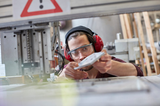 Male designer wearing ear protectors, examining prototype in workshop