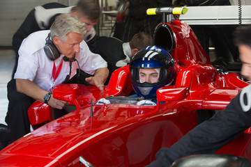 Manager talking to formula one race car driver in repair garage