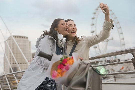 Enthusiastic, smiling women friends taking selfie camera phone near Millennium Wheel, London, UK