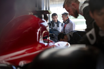 Manager and formula one race car driver talking in repair garage