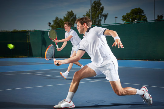 Young male tennis doubles players playing tennis, hitting the ball on blue tennis court