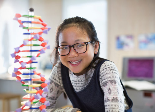 Portrait smiling, confident girl student next to DNA model in classroom