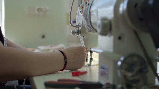 Closeup of woman's hands with manucure sewing green fabric with a sewing machine. Women's hands sew on a sewing machine. Fashion, creation and tailoring. High angle view