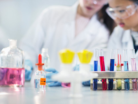 Girl students conducting scientific experiment behind test tubes and bottles in laboratory classroom