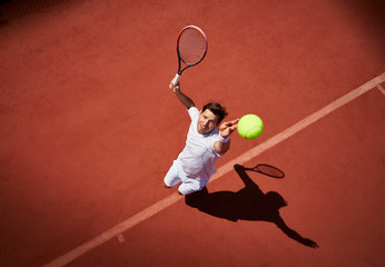 Overhead view young male tennis player playing tennis, serving the ball on sunny tennis court