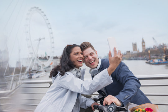 Smiling couple tourists taking selfie camera phone on bridge near Millennium Wheel, London, UK