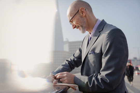 Businessman checking smart watch on sunny urban sidewalk, London, UK