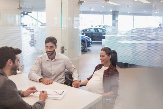 Car salesman talking to pregnant couple in car dealership office