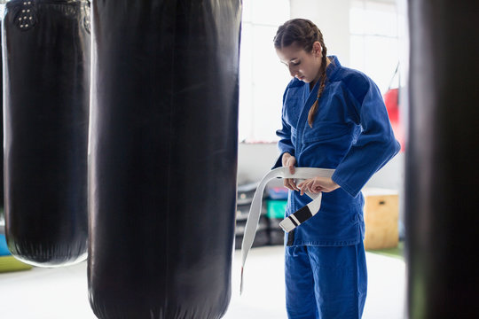 Young woman tying judo belt at punching bags in gym