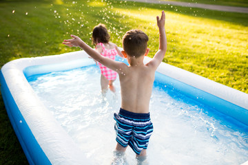 Preschool brother sister playing splashing in inflatable swimming pool