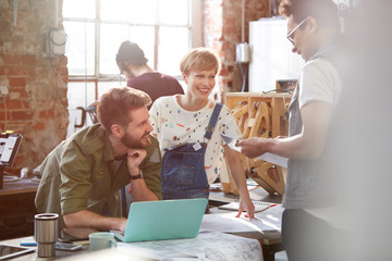 Designers meeting, discussing plans at laptop in workshop