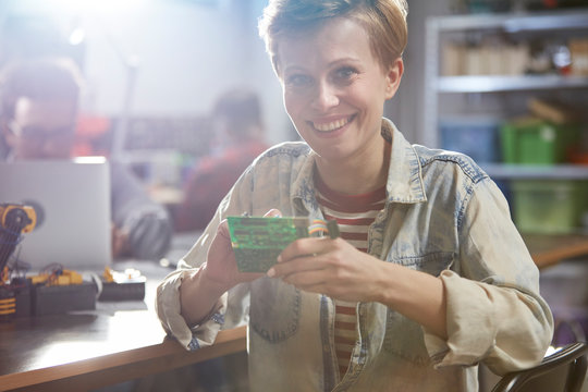 Portrait smiling female engineer assembling circuit board in workshop