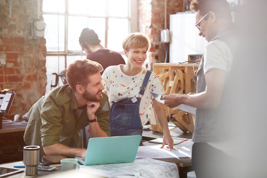Designers meeting, discussing plans at laptop in workshop