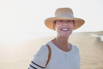 Portrait smiling mature woman wearing straw hat on sunny summer beach