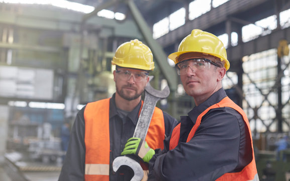 Portrait confident, tough male workers with large wrench in factory