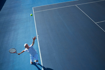Overhead view young male tennis player playing tennis, serving the ball on sunny blue tennis court