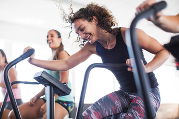 Smiling, playful young woman using elliptical bike in gym
