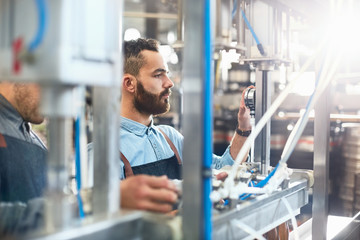 Male brewer adjusting dial on bottling machine in brewery
