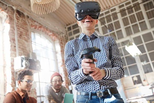 Smiling female computer programmer testing virtual reality simulator glasses joystick
