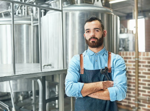 Portrait confident male brewer in front of vat in brewery