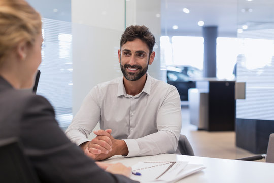 Smiling male customer listening to car saleswoman in car dealership office