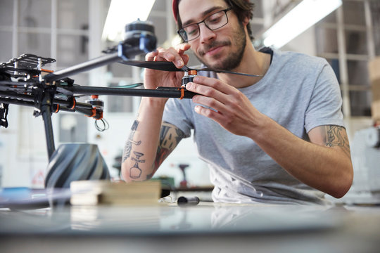 Male designer with tattoos assembling drone in workshop