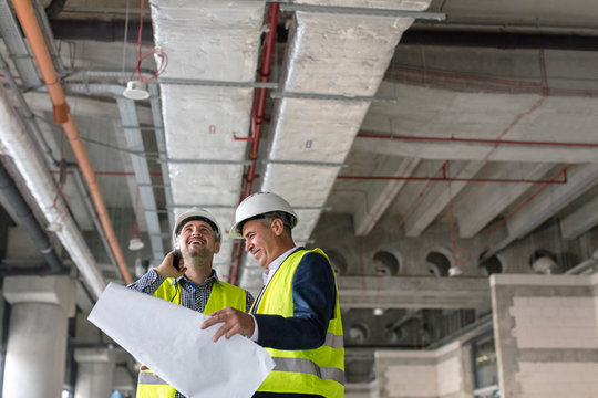 Male engineers with flashlight and blueprints at construction site