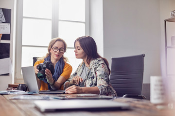 Female photographers with digital camera working at laptop in office