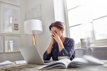 Tired, stressed businesswoman at laptop with head in hands