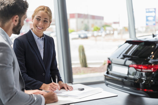 Car saleswoman male customer signing contract paperwork in car dealership showroom