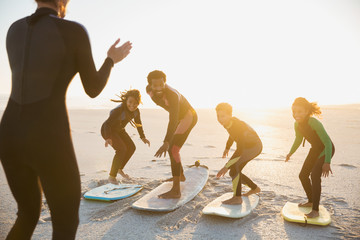 Surfer instructor teaching family on surfboards surfing on sunny summer sunset beach