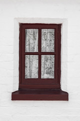 Generic old red wooden window frame against a white wall with delicate net curtains inside.