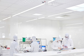 Engineers in clean suits using machinery in fiber optics research testing lab