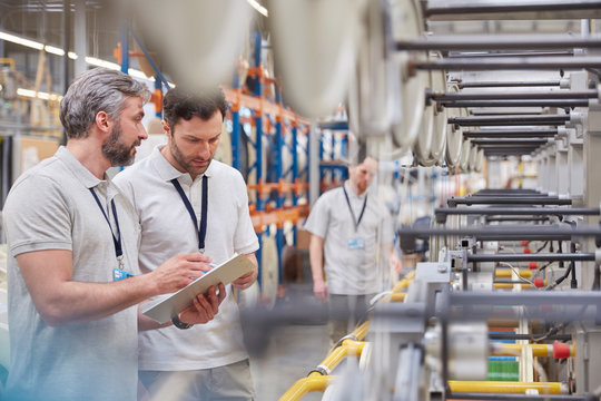 Male supervisor worker with clipboard talking in fiber optics factory