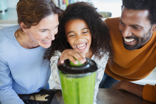 Laughing multi-ethnic family making healthy green smoothies in blender in kitchen