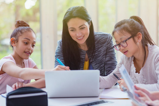Female teacher and girl students researching at laptop in library