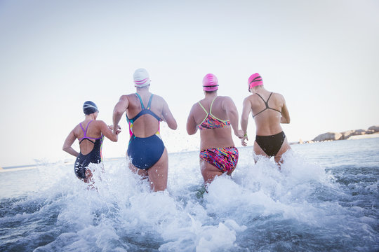 Female open water swimmers running and splashing in ocean surf