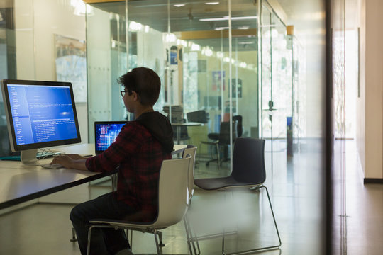 Focused boy student programming at computer in dark classroom